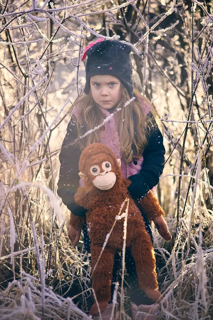 a girl holding a stuffed animal in a snowy forest